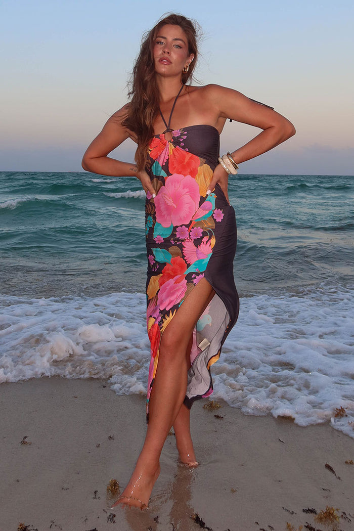 Woman in a colorful floral dress standing on a beach with ocean waves in the background. Spell, Beach bar dress, floral dress, boho dress, byron bay