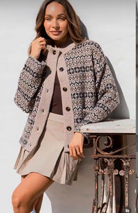 Woman wearing a patterned cardigan over a dress, standing outdoors.
